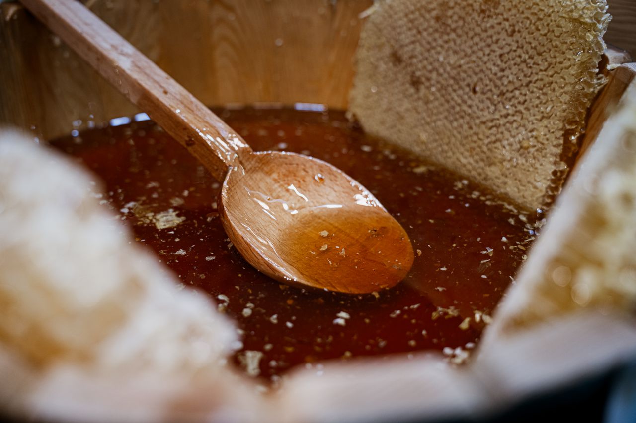 who-we-are Close-up of fresh honey and honeycomb with a wooden spoon in a rustic wooden bowl.