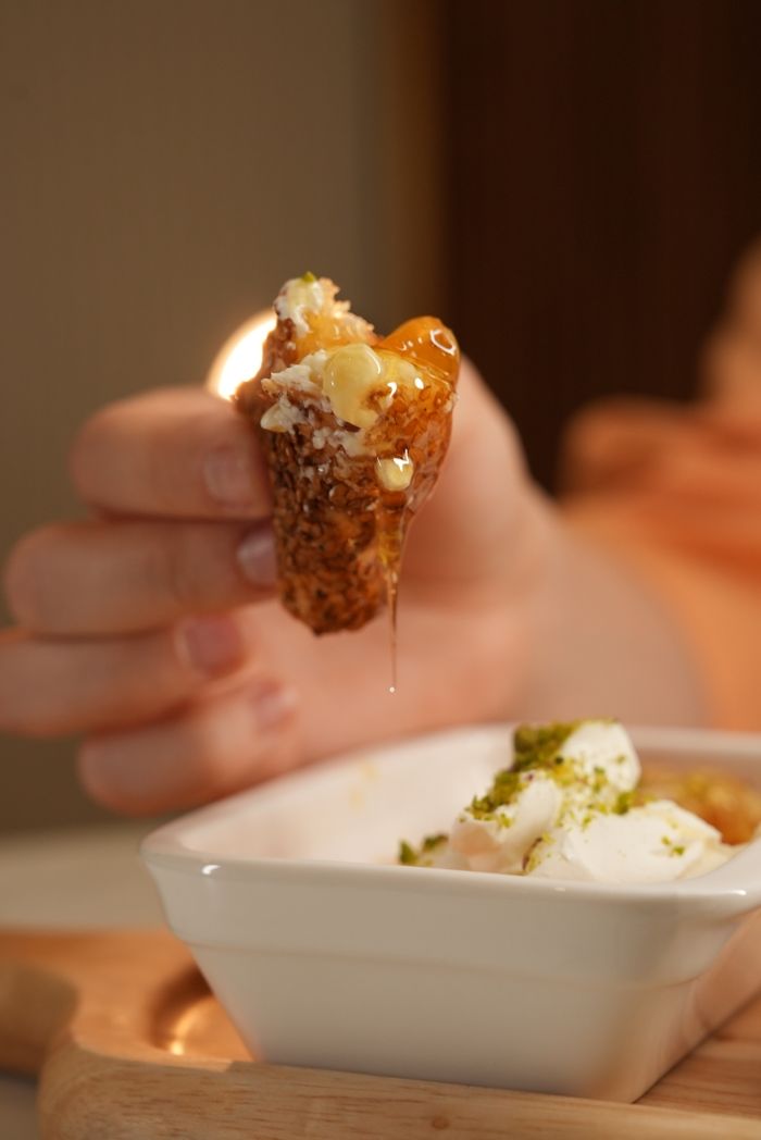 our-story Hand holding a sweet dessert dipped in honey, ready to eat.