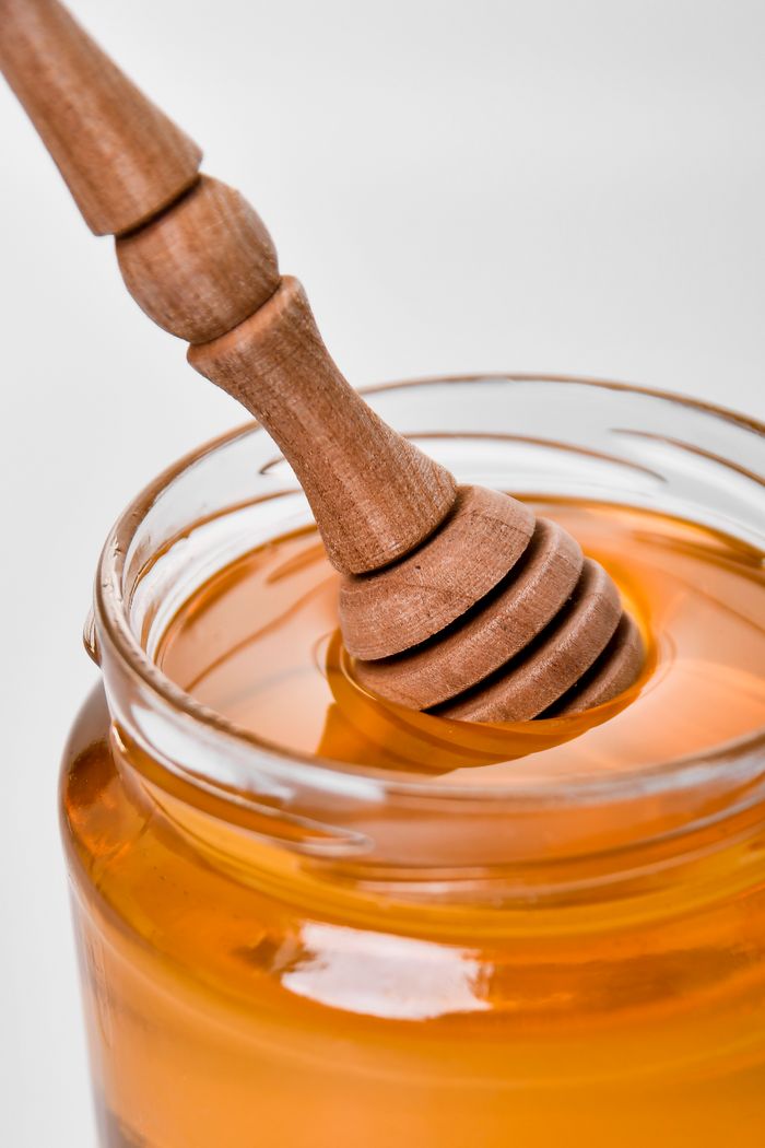 services-02 Close-up of golden honey in a glass jar with a wooden honey dipper.